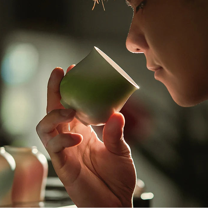 Person holding a green ceramic cup with 'MUVNA' branding in the corner.